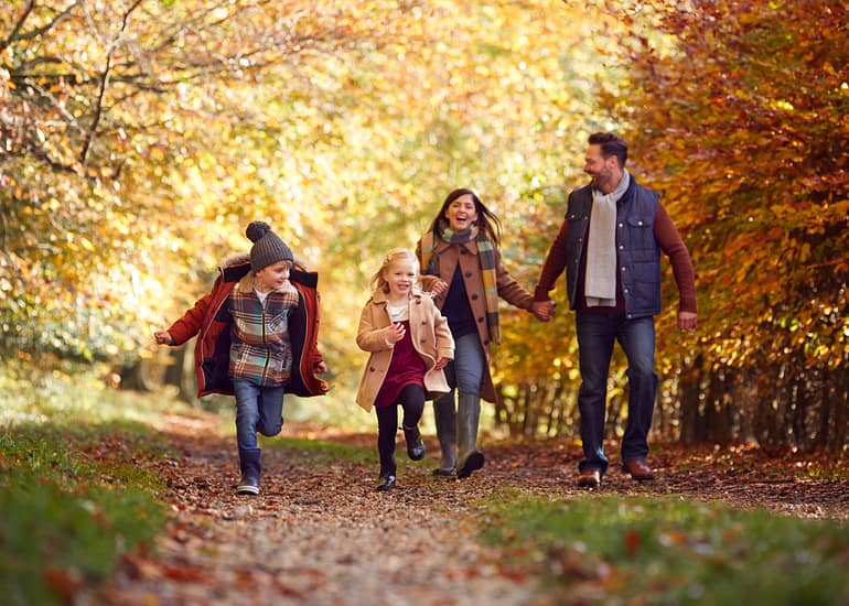Family Walking Along Track In Autumn Countryside With Children Running Ahead